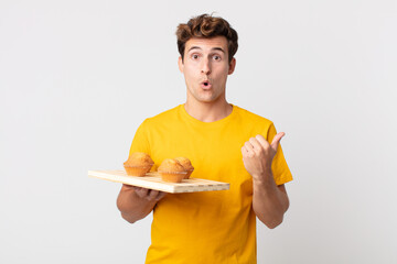 young handsome man looking astonished in disbelief holding a muffins tray