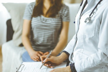 Obraz premium Unknown woman doctor and patient discussing current health examination while sitting in cozy living room. Stay at home concept during Coronavirus pandemic and self isolation quarantine