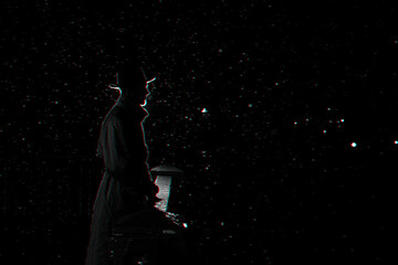 dark silhouette of a man in a hat at night in the rain in the city