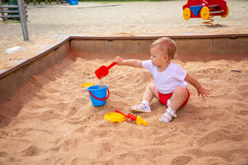 Adorable toddler girl playing with sand on sandbox in playground
