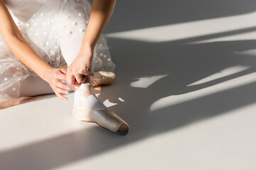 Cropped view of ballerina wearing pointe shoe on grey background with light