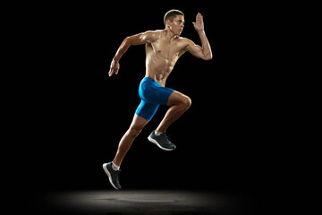 Fototapeta na wymiar Leader, champion. Young professional male athlete, runner training isolated on dark studio background. Muscular, sportive man. Concept of sport, healthy lifestyle