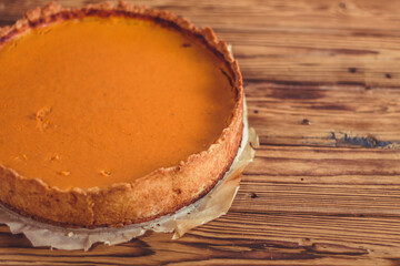 Orange spicy autumn pumpkin pie. Shortcrust vanilla tart with sweet pumpkin cream on brown wooden background with small sliced pumpkins walnuts oak leaves and seeds. Free copy space. Top view