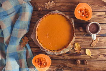 Orange spicy autumn pumpkin pie. Shortcrust vanilla tart with sweet pumpkin cream on brown wooden background with small sliced pumpkins walnuts oak leaves seeds cacao cup. Free copy space Top view