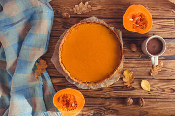 Orange spicy autumn pumpkin pie. Shortcrust vanilla tart with sweet pumpkin cream on brown wooden background with small sliced pumpkins walnuts oak leaves seeds cacao cup. Free copy space Top view