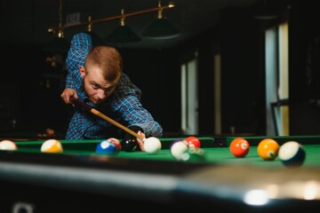 Fototapeta premium Young man playing billiards in the dark billiard club