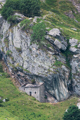 Mountain house in the middle of the alps. Summer in the green mountain with a little house. Alpine mountains with a play of light and shadow of the clouds.
