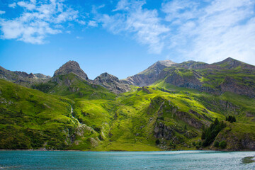Mountain lake in the middle of the alps. Summer in the green mountain with a blue lake. Alpine mountains with a play of light and shadow of the clouds.