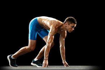 Side view of young professional male athlete, runner preparing to start isolated on dark studio background. Muscular, sportive man. Concept of sport, healthy lifestyle