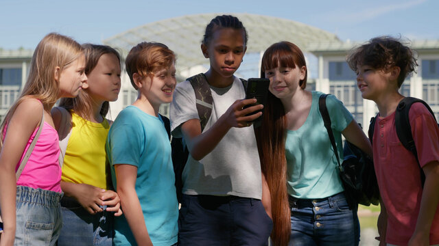Multiethnic teen children outdoors watching video on smartphone together