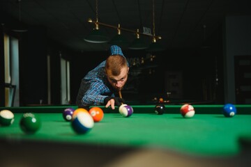 Young man playing billiards in the dark billiard club