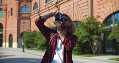 Fototapeta premium Young traveler photographer man smiling happy using vintage camera at city street