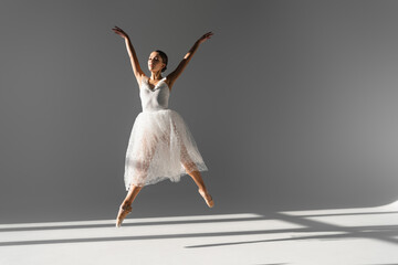 Young ballerina dancing and jumping on grey background with sunlight