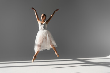 Fototapeta premium Young ballerina dancing and jumping on grey background with sunlight