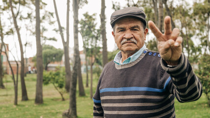 elderly man giving a sign of peace and love, enjoying the outdoors in the park, taking a walk.