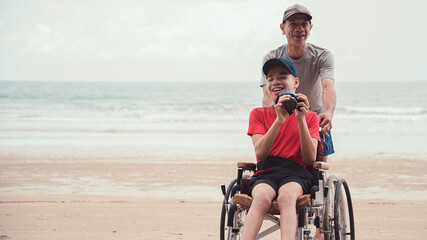 Happy disabled teenage boy smile face on wheelchair holding a camera with father, Activity outdoors...