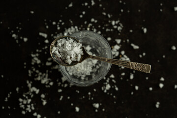 Salt, pure sea salt with no additives. Coarse white salt on dark black background with a spoon.