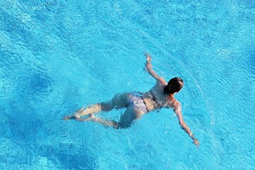 Girl in a swimsuit swimming in the pool water, top view. Water sports, beach vacation