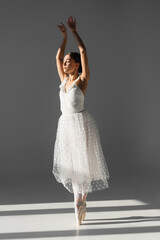 Naklejka premium Ballerina dancing with closed eyes on grey background