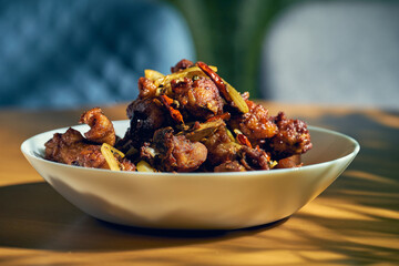 Fried chicken in chili sauce with onions in a white plate. Wood background. Chinese cuisine