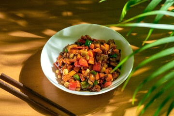Chicken in sweet and sour sauce, with Sichuan pepper, peanuts in a white bowl. Wood background. Chinese cuisine