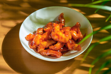 Chicken in sweet and sour sauce, with Sichuan pepper, peanuts in a white bowl. Wood background. Chinese cuisine