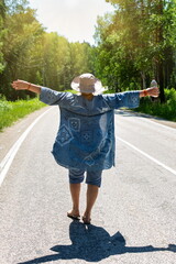 An elderly woman is walking along the road with a drink to quench her thirst and is enjoying a...
