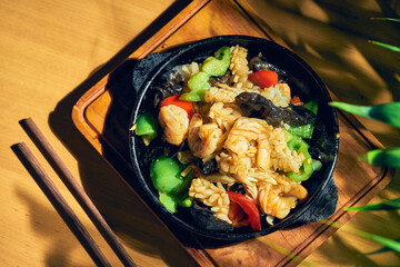 Fried seafood (shrimp, mussels, squid) in sweet and sour sauce, with Sichuan pepper in a skillet. Wood background. Chinese cuisine