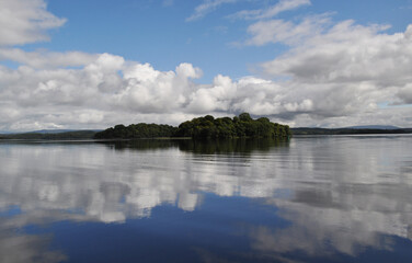 Fototapeta premium Reflection of an island in a lake with clouds on the horizon