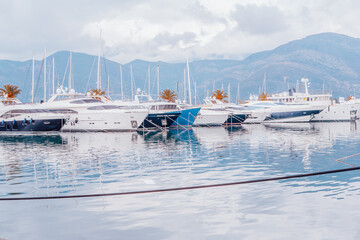 Marina with yachts on the background of mountains on a cloudy day. The prows of large yachts