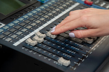 A woman's hand with a white manicure operates a mixing console on the radio. Close up
