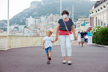 Grandmother and toddler child, walking hand in hand in the center of Monaco, summer 2021, medical...