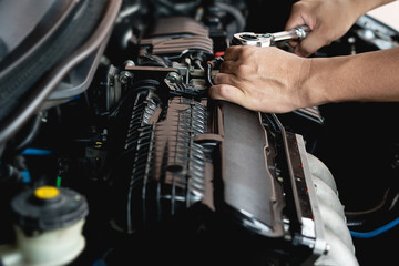 Fototapeta na wymiar Closeup spanner in hand male mechanic repairs car in garage. Car maintenance and auto service garage concept