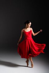 Naklejka premium Young brunette ballerina in red dress dancing on black background