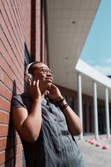 Fototapeta premium African happy woman in wireless headphones listening to music and enjoying the sunny weather outdoors