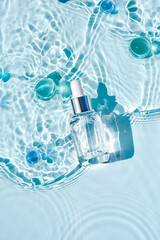 Mockup of cosmetic glass blue bottle with pipette and serum on water surface with waves....
