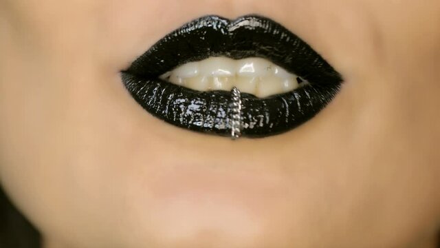 Closeup of a beautiful woman lips with beautiful black makeup and piercing sending air kiss . Close up of girl's mouth having flirty emotions and sending air kiss 