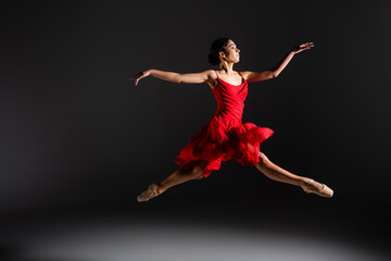 Side view of ballerina in red dress jumping on black background