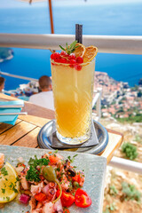 Orange fruit cocktail with snacks on a wooden table over Dubrovnik cityscape view. Croatia.