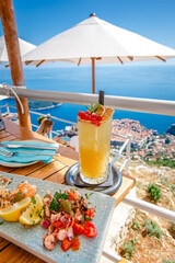 Orange fruit cocktail with snacks on a wooden table over Dubrovnik cityscape view. Croatia.