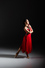 Naklejka premium Side view of classical dancer in pointe shoes standing on black background