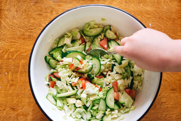 salad with tomato, cabbage and cucumber in a large white bowl on a wooden table