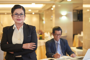 Portrait of elegant senior businesswoman in glasses crossing arms and looking at camera, her...