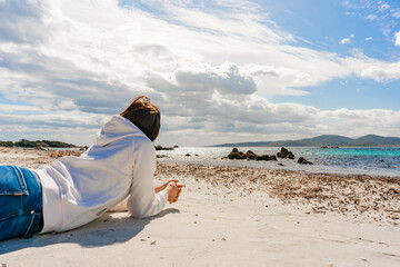 Pensive young unrecognizable woman lying on the elbows on the sand of winter ocean sea looking...