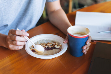 Young smiling blonde woman freelancer working on notebook on table at cafe. Girl student girl studying on online course. Woman having porridge on breakfast in the cafe