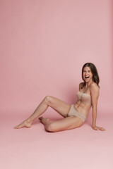 Naklejka premium Portrait of young beautiful tanned woman in lingerie posing isolated over pink studio background. Natural beauty concept.