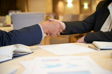 Close-up image of senior entrepreneurs shaking hands after discussing reports with charts and diagrams