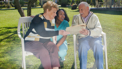 Young african female nurse smiling outdoor with elderly retired couple, talking to them in the hospital garden using tablet