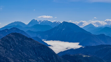 Fototapeta premium A panoramic view from the top of Alpine peak in Austria. The whole area is shrouded in thick clouds. A few peaks popping out from the clouds. High mountain chains in the back. Carpet from the clouds
