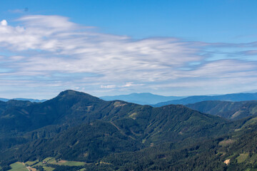 A panoramic view on the Alpine valley in Austria. High mountains around. The slopes are partially overgrown with small bushes, higher parts baren. Small lake at the bottom. Clear and sunny day.